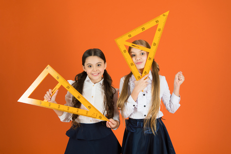 Getting back to the square roots. Little girls ready for geometry lesson. Small girls are back to school. School children with measuring instruments. Cute schoolgirls holding triangles for lesson.の写真素材