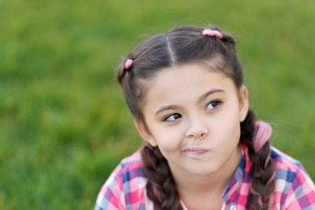 Springtime concept. Cute daydreamer. Girl little kid spend leisure outdoors in park. Girl sit on grass in park. Child enjoy spring sunny weather while sitting at meadow in park. Park and garden.の写真素材