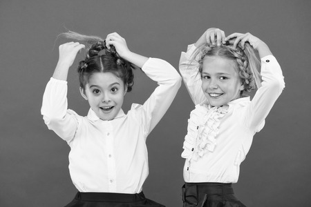 Keep hair braided for tidy look. Kids pupils play with long braided hair. Hairdresser salon. Hairstyles which suits to formal school style. Appropriate hairstyle. Girls long braids red background.の写真素材