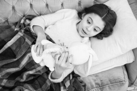 Kid lay bed and hug bunny toy couch pillow blanket background top view. Girl child wear pajamas hug bunny.の写真素材