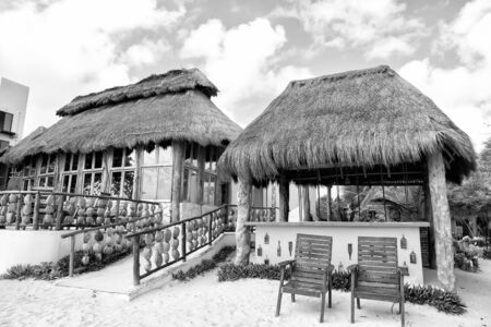 exotic beach bar with house building and straw roof near chairs on sand outdoor on blue cloudy sky...