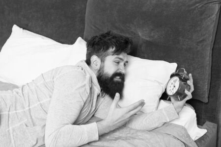Bearded man hate alarm clock while lying in bed at home.