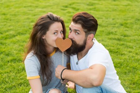 Given his heart to her. Sensual couple in love with prop heart on green grass. woman and man holding valentines heart on stick. One heart two souls.の写真素材