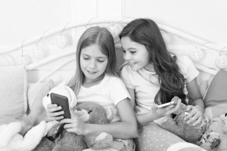 Sharing good news. Little girls use smartphone in bed. Ordering gifts for Christmas and New Year by phone. Happy little children with mobile phone. Merry Christmas and Happy New Year greetingsの写真素材