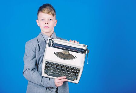 Retrospective study. Boy hold retro typewriter on blue background. What to do with this thing. Out of date. I need modern gadget instead this retro. Outdated gadget. Retro and vintage. Yard saleの写真素材
