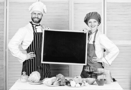 Making good food. Chef and cook helper teaching master class. Couple of man and woman holding empty blackboard in cooking school. Master cook and prep cook giving cooking class, copy spaceの写真素材