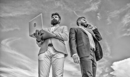 Always in touch. Men well groomed businessman holds laptop partner speak phone blue sky background....