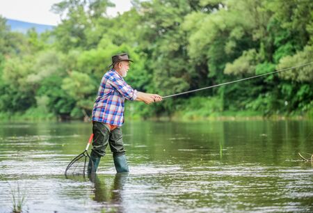 Mature man fishing. Retired fisherman. Male leisure. Fisherman with fishing rod. Activity and hobby. Fishing freshwater lake pond river. Happiness is rod in your hand. Senior man catching fishの写真素材