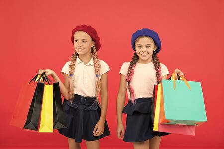 Children pupils satisfied by shopping red background. Obsessed with shopping and clothing malls. Shopaholic concept. Signs you are addicted to shopping. Kids cute schoolgirls hold bunch shopping bagsの写真素材