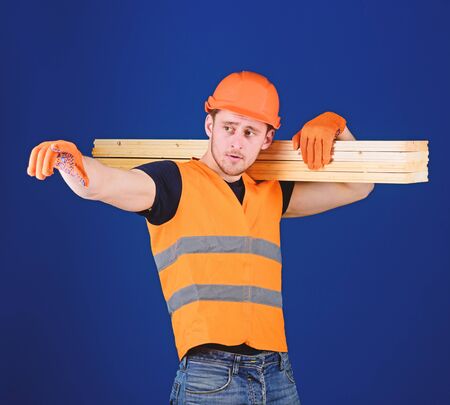 Man in helmet, hard hat and protective gloves pointing direction, blue background. Carpenter,...