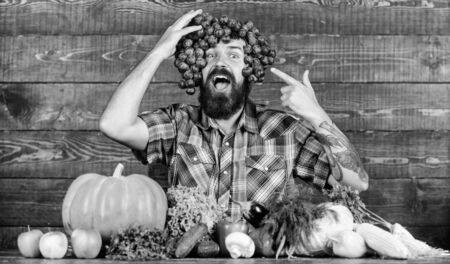 Farming concept. Man hold grapes wooden background. Farmer bearded guy with homegrown harvest grapes put on head. Farmer proud of grapes harvest. Fresh organic harvest. Grapes from own gardenの写真素材