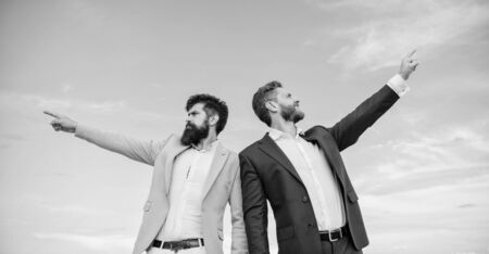 Businessmen bearded faces stand back to back sky background. Men formal suit managers pointing at opposite directions. Changing course. New business directions. Developing business directionの写真素材