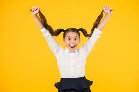 Easy hair for school. Happy small girl holding long brunette hair on yellow background. Styling hair...