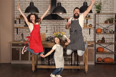 Prepare delicious meal. Breakfast time. Family having fun cooking together. Teach kid cooking food. Cooking together. Family mom dad and daughter wear aprons stand in kitchen. Cooking food conceptの写真素材