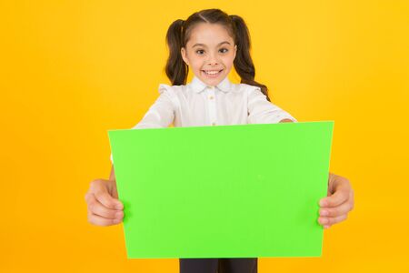 Being given a home work. Little child holding empty sheet for examination work on yellow background. Small girl with blank green paper for project work or research. Paper work, copy spaceの写真素材