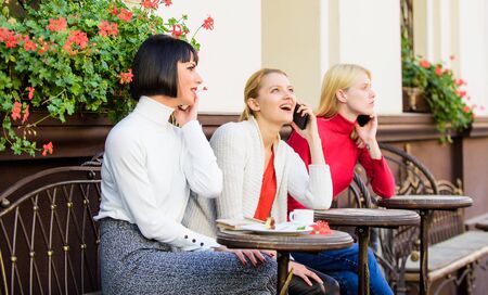 Friends sit in coffee shop and enjoy talk. Obsessed with speaking. Using digital devices. Group women cafe terrace. Friendship meeting. Mobile addicted. Mobile conversation. Girls with mobile phonesの写真素材