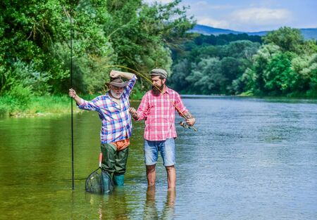 Fishing freshwater lake pond river. Mature man with friend fishing. Summer vacation. Happy cheerful people. Fisherman with fishing rod. Bearded men catching fish. Family time. Activity and hobbyの写真素材