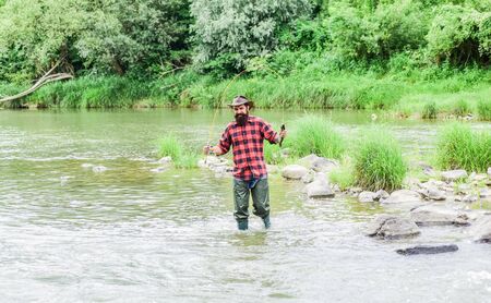Fisher masculine hobby. Fish on hook. Brutal man stand in river water. Man bearded fisher. Fishing requires to be mindful and fully present in moment. Fisher fishing equipment. Rest and recreationの写真素材