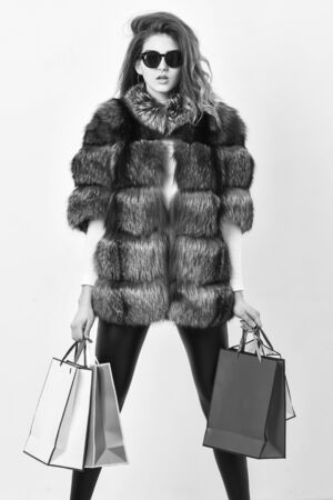 Buy with discount on black friday. Shopping with promo code. Woman shopping luxury boutique. Girl wear sunglasses and fur coat shopping white background. Lady hold shopping bags. Discount and saleの写真素材