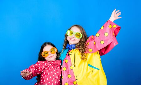 family bonds. Small girls in raincoat and glasses. happy small girls in colorful rain coat. rain protection. Rainbow. autumn fashion. cheerful hipster children, sisterhood. having fun. Totally freeの写真素材