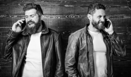Men with smartphones discuss business. Mobile conversation and connect. Business call. Men brutal bearded hipster in fashionable leather jackets use mobile phone. Online business. Modern technologyの写真素材