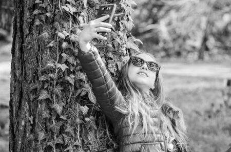 happy child in park. selfie time. Natural beauty. Childhood happiness. summer nature. little girl make selfie in park. Spring holiday. Green environment. climbing plant on tree with ivy leavesの写真素材
