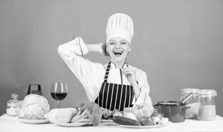 Woman chef cooking healthy food. Gourmet main dish recipes. Girl in hat and apron. Delicious recipe concept. Cooking healthy food. Fresh vegetables ingredients for cooking meal. Lets start cookingの写真素材