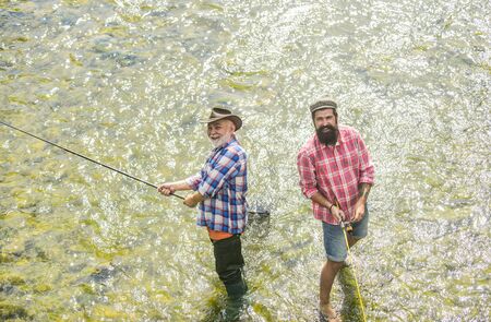 Active sunny day. Fishermen fishing equipment. Hobby sport activity. Fishermen friends stand in river. Fish normally caught in wild. Summer leisure. Men bearded fishermen. Weekends made for fishingの写真素材