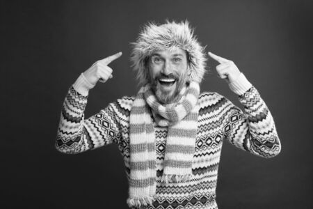 Wearing some key winter accessories. Bearded man in sweater and scarf pointing at hat. A winter ensemble protects him from cold. Mature fashion model in cold weather style. Winter wardrobe for manの写真素材