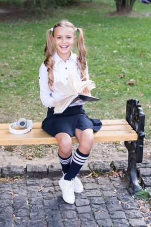 Time to study. Schoolgirl reading book. Little genius. Schoolgirl relaxing sit bench with book. Studying in school yard. Smart schoolgirl. Student adorable child in formal uniform relaxing outdoorsの写真素材