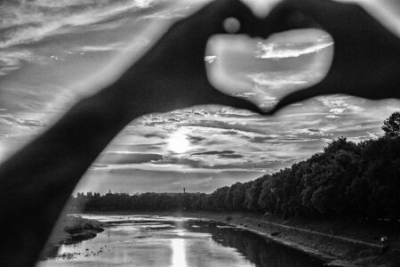 Sunset sunlight romantic atmosphere. Heart gesture in front of sunset above river. Hands in heart shape gesture symbol of love and romance. Romantic date ideas. Idea honeymoon travel. Vacation resortの写真素材