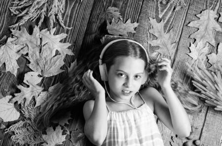 Autumn melody concept. Child listen music relaxing top view. Autumn music playlist. Best songs about fall. Enjoy music and relax. Happy childhood. Kid girl wooden background listen music headphonesの写真素材
