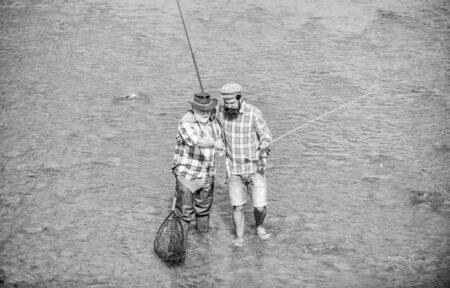 Coming together. male friendship. family bonding. summer weekend. mature men fisher. two happy fisherman with fishing rod and net. hobby and sport activity. Trout bait. father and son fishingの写真素材