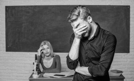 He is so shy. Male student with examiner at examination. High school student saying lesson. Handsome man standing in classroom with teacher. University or college student covering faceの写真素材