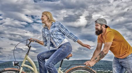 Girl cycling while man support her. Support helps believe in yourself. Feel impulse to start moving. Woman rides bicycle sky background. Push and promoting. Impulse to move. Man pushes girl ride bikeの写真素材