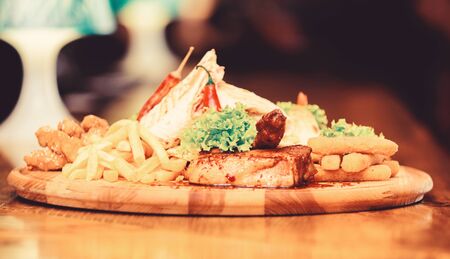 Restaurant food. Wooden board with lot french fries fish sticks burrito and meat steak served with...
