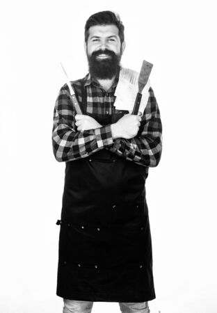 Using a barbecue set. Confident grill cook. Bearded man holding grill gripper tools. Hipster in apron with metal utensils for barbecue grill. Preparing food on grillの写真素材