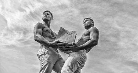 Guys attractive twins carry shopping bag made out of brown paper. Men muscular athletes hold shopping bag sky background. Brothers buy eco healthy products. Hot sales and discount. Sales seasonの写真素材