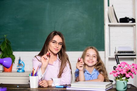 Little girl and woman sit at desk. School education. Studying together. Help with homework. Homework project. Sister helping with learning. Teacher kind lady with pupil. Doing homework with momの写真素材