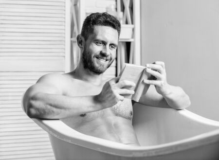 Sexy man in bathroom reading. Macho naked in bathtub. relaxation concept. man has muscular body. Wash off foam with water carefully. book lover. macho enjoying book in bath. happy manの写真素材
