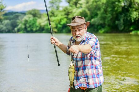 Fisherman with fishing rod. Activity and hobby. Fishing freshwater lake pond river. It is not sport, it is obsession. Senior bearded man catching fish. Mature man fishing. Retired bearded fishermanの写真素材