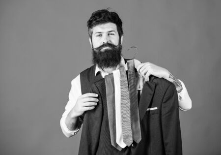 Guy choosing necktie. Perfect necktie. Shopping concept. Shop assistant or personal stylist service. Stylist advice. Matching necktie with outfit. Man bearded hipster hold neckties and formal suitの写真素材