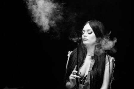 Nicotine addiction. Attractive busty brunette smoking vaping device. Girl vaping. Hookah bar. Electronic cigarette. Fashion girl vaping. Relaxing with hookah. White cloud of smoke. Vaping is sexyの写真素材