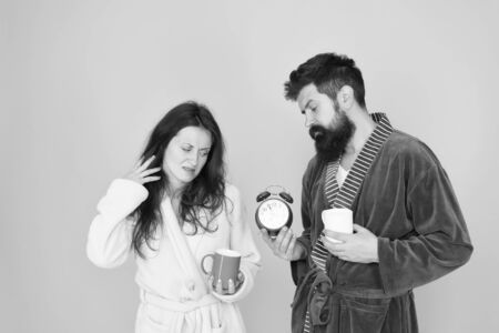 Its coffee time. Couple in bathrobes with mugs. Man with beard and sleepy woman enjoy morning coffee or tea. Guy in bath clothes hold tea coffee. Breakfast concept. Every morning begins with coffeeの写真素材
