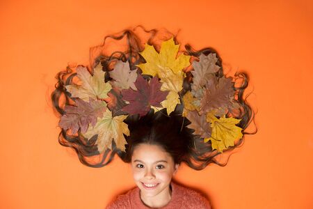 Creative way to wear autumn leaves. Little child with colorful leaves in long brunette hair. Autumn...