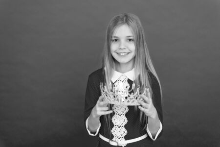 Lady little princess. Girl cute smile hold crown while stand red background. Best award for me. Kid hold golden crown symbol of princess. Happy childhood concept. Every girl dreaming become princessの写真素材