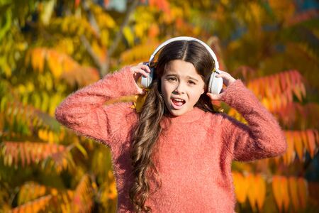 Listening audio best way help child improve vocabulary. Kid girl relaxing near autumn tree with headphones. Autumn walks with nice songs. Music for autumn mood. Listening song. Enjoy music fall dayの写真素材