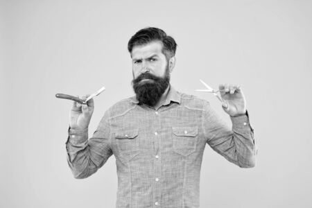 Barbershop offer range of packages for groom. Bearded man work in barbershop. Hipster hold barber tools yellow background. Barbershop concept. Beard shaping and styling in barbershopの写真素材
