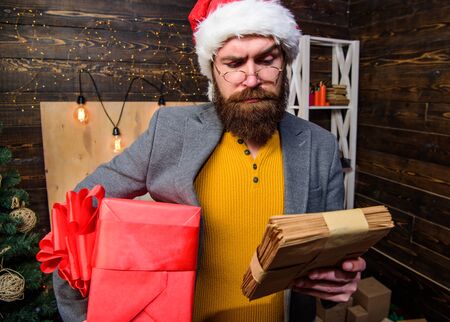 Man bearded hipster wear santa hat hold bunch of letters and gift box. Gifts delivery service. Letter for santa claus. Man mature bearded with eyeglasses received post for santa. Post for santa clausの写真素材
