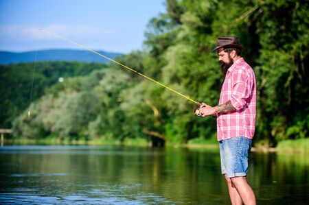 weekend relax. mature bearded man with fish on rod. hipster fishing with spoon-bait. fly fish hobby. Summer fishery activity. successful fisherman in lake water. big game fishing. relax on natureの写真素材